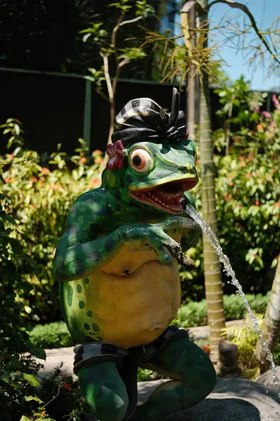 Geleneksel Bali başlığı gibi görünen yeşil kurbağa heykeli ağzından suyu bir gölet veya bahçe özelliğine püskürtür.