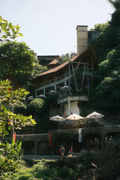 Kemenuh, Bali - 27 Nisan 2025: Omma Günü Kulübü olarak tanımlanan çarpıcı bir mimari kompleks, Bali 'deki Tegenungan Şelalesi' nde sarp, canlı yeşil bir yamaçta inşa edilmiştir. Birden fazla seviye ve belirgin kıvrımlı çatı yapısına sahiptir.