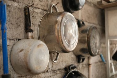 Değişik büyüklükteki metal tencere ve tavaların kaba, dokulu bir duvarda asılı olduğu taşralı mutfak sahnesi geleneksel ya da kırsal yemek yapma hissi uyandırıyor.