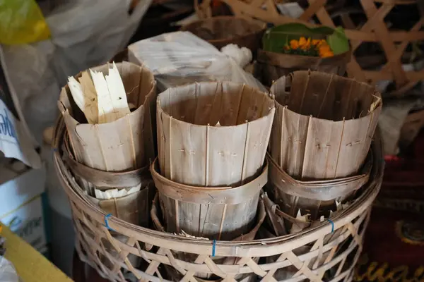 Çeşitli doğal, muhtemelen törensel, dokunmuş palmiye yapraklarından ya da benzer organik malzemelerden yapılmış kaplar, kadife çiçekleri ya da açık renkli yapraklardan oluşan bir koleksiyon.