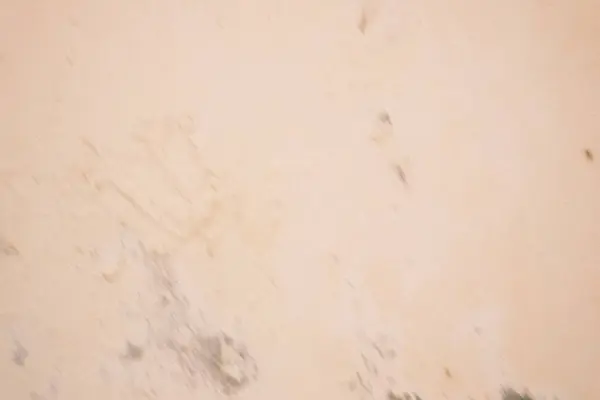 Yakın plan çekimde, soluk, açık sarı-kahverengi tonlarda, eskimiş alçı ya da betonu andıran desenli bir duvar yüzeyi ortaya çıkıyor..