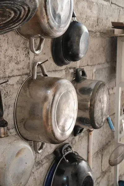 Değişik büyüklükteki metal tencere ve tavaların kaba, dokulu bir duvarda asılı olduğu taşralı mutfak sahnesi geleneksel ya da kırsal yemek yapma hissi uyandırıyor.