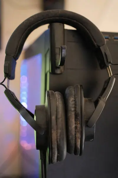 Bir çift eski, ağır giyilmiş siyah kulaklıklar koyu bir stantta asılı, kulaklıklarda görünür toz ve renk değişimi, uzun vadeli kullanım öneriyor