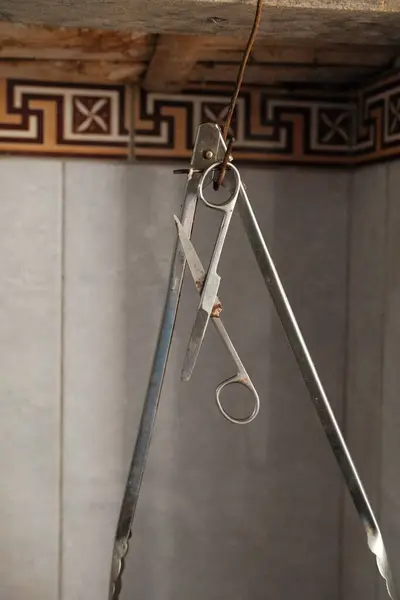 Bir çift eski, büyük metal maşa yakın çekim bir tel daha küçük bir makas ile asılı, açık renkli karo duvara karşı dekoratif süslemeli