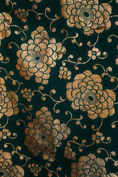 Karmaşık altın brokar çiçek desenleriyle süslenmiş koyu yeşil bir kumaşın detaylı bir yakın çekimi.