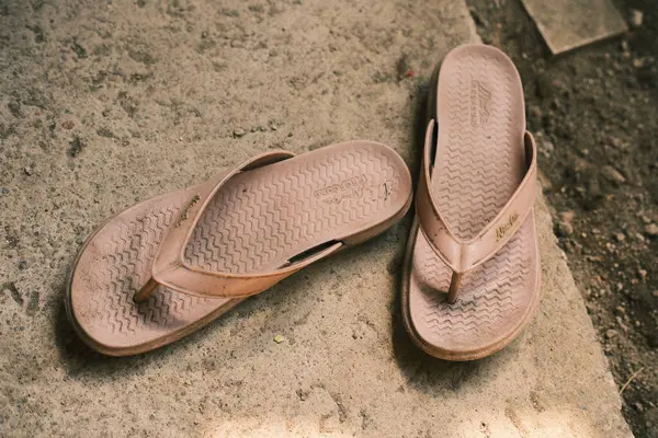 Denpasar, Bali - 02 Mayıs 2025: Dokulu tabanlı açık kahverengi kauçuk parmak arası terlikler, her gün ya da her gün açık havada giyildiğini düşündüren sert beton bir yüzey üzerindedir.