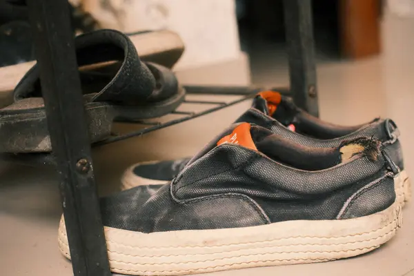 Kirli beyaz tabanlı, eskimiş koyu renk ayakkabılar ve metal bir ayakkabı rafında dinlenen bir çift sandalet..