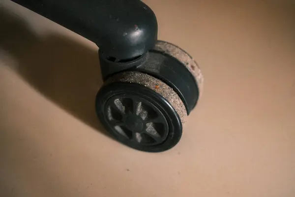 Yakın çekim, iyi kullanılmış bir ofis sandalyesi tekerleğinin dokulu yüzeyini çeker, aşınma ve yırtık izleri gösterir, fonksiyonel bileşenini ve günlük kullanımını vurgular.