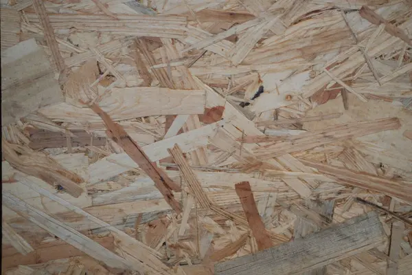 Bir Oriented Strand Board (OSB) yüzeyinin tam kare yakın çekimi, baskılı ahşap pullarından oluşan rustik dokusunu, endüstriyel veya inşaat arka planları için ideal olarak sergiliyor.