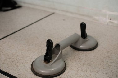 Siyah saplı ağır gri çift emici bir bardak kaldırıcı, cam veya diğer düz malzemeler için tasarlanmış hafif benekli bir yüzeye dayanır..