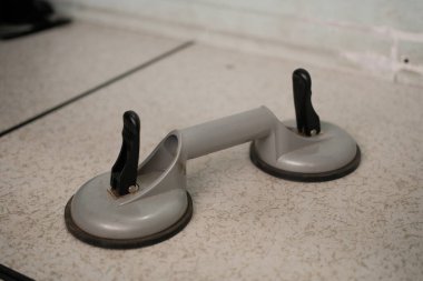 Siyah saplı ağır gri çift emici bir bardak kaldırıcı, cam veya diğer düz malzemeler için tasarlanmış hafif benekli bir yüzeye dayanır..