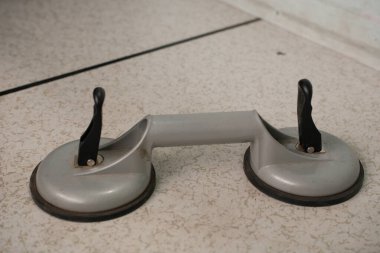 Siyah saplı ağır gri çift emici bir bardak kaldırıcı, cam veya diğer düz malzemeler için tasarlanmış hafif benekli bir yüzeye dayanır..