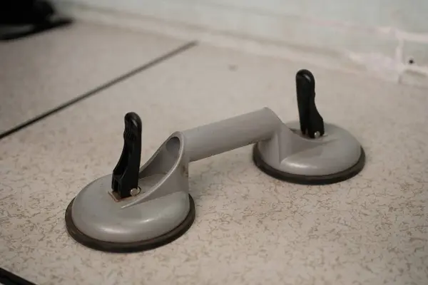 Siyah saplı ağır gri çift emici bir bardak kaldırıcı, cam veya diğer düz malzemeler için tasarlanmış hafif benekli bir yüzeye dayanır..