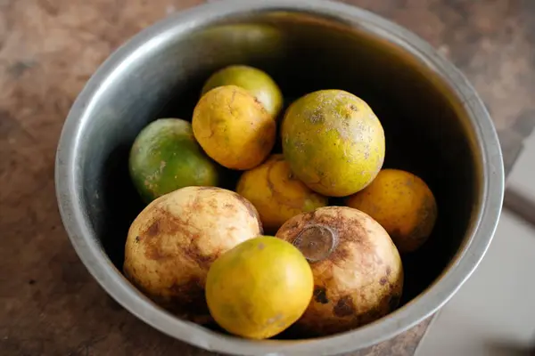Tepeden çekilen bir fotoğraf, yeşil ve sarı portakalların yanı sıra guavaları yakalıyor. Hepsi de kırsal bir metal kasede toplanıyor. Bu da taze ve doğal bir ürün olduğunu gösteriyor.