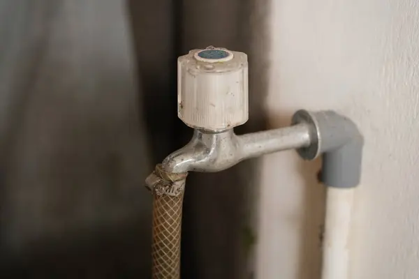 Eski, yıpranmış bir açık hava musluğunun yakın plan görüntüsü. Buruşuk bir hortum güvenli bir şekilde bağlanmış, bulanık bir arka plan üzerine kurulmuş..