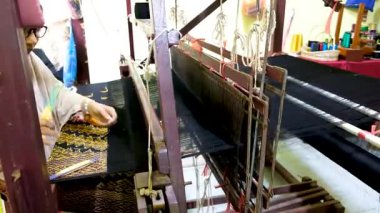 Pekanbaru, Endonezya - 26 Şubat 2025: Kadın dokumacı, Kampung Bandar Tenun Evi 'nde geleneksel dokuma tezgahı kullanarak Riau Malay' ın şarkı sözlerini örüyor.