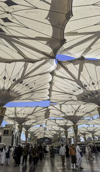 Medine, Suudi Arabistan - 6 Mart 2024: Seyyahlar, Hz. Muhammed el-Mecid an-Nabawi 'nin ana camisine dev şemsiyeler altında yürür ve namaz kılmaya hazırlanırlar..