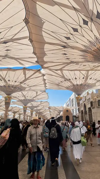 Medine, Suudi Arabistan - 6 Mart 2024: Seyyahlar, Hz. Muhammed el-Mecid an-Nabawi 'nin ana camisine dev şemsiyeler altında yürür ve namaz kılmaya hazırlanırlar..