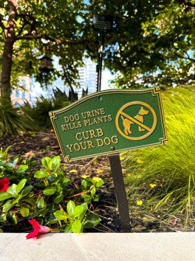 Los Angeles, California, ABD - Köpek idrarı Bitkileri Öldürdü, Köpeğinizi Kaldırın İşaretini Kaldırın, Yeşil ve Altın Metal Üstü Çizili Köpek, Pembe Çiçekler, Ağaçlar, Çalılıklar, Soluk Mavi Skyline