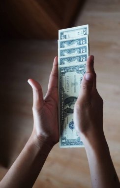 Bir, iki ve beş dolarlık banknotlar da dahil olmak üzere, düşük kalite Amerikan dolarlarını tutan bir kadının yakın çekimi. Odak noktası para birimi detayları ve el ele tutuşması..