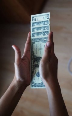 Bir, iki ve beş dolarlık banknotlar da dahil olmak üzere, düşük kalite Amerikan dolarlarını tutan bir kadının yakın çekimi. Odak noktası para birimi detayları ve el ele tutuşması..