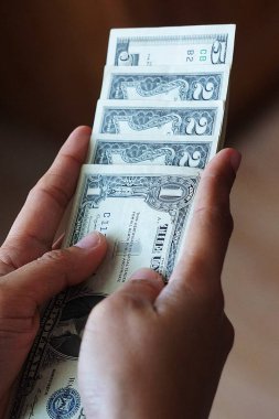 Bir, iki ve beş dolarlık banknotlar da dahil olmak üzere, düşük kalite Amerikan dolarlarını tutan bir kadının yakın çekimi. Odak noktası para birimi detayları ve el ele tutuşması..