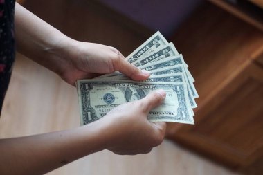 Bir, iki ve beş dolarlık banknotlar da dahil olmak üzere, düşük kalite Amerikan dolarlarını tutan bir kadının yakın çekimi. Odak noktası para birimi detayları ve el ele tutuşması..