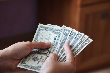 Bir, iki ve beş dolarlık banknotlar da dahil olmak üzere, düşük kalite Amerikan dolarlarını tutan bir kadının yakın çekimi. Odak noktası para birimi detayları ve el ele tutuşması..