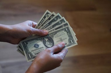 Kadınların elleri kahverengi arka planda Amerikan dolarlarını tutuyor. Para ve finans, doğal ve sıcak bir ortamda..