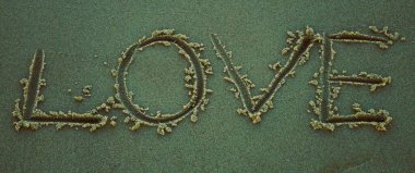 The word LOVE written in sand on the beach, romantic atmosphere, spring or summer vibes, waves in the background, seaside vacation, love and relaxation in nature.