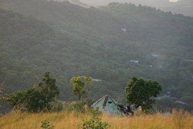 Palawan 'da bir dağ zirvesinde bulunan muşambadan yapılmış küçük bir sığınak geniş ormanlara ve sıradağlara bakıyor. Günbatımının sıcacık parıltısı gökyüzünü altın rengine boyuyor..