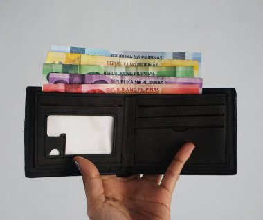 Filipin banknotları, 1000, 500, 200, 100 ve 50 peso olan bir kadının elinde duran kahverengi cüzdan. Resim günlük hayatta para biriktirmeyi ve kazanmayı temsil eder.