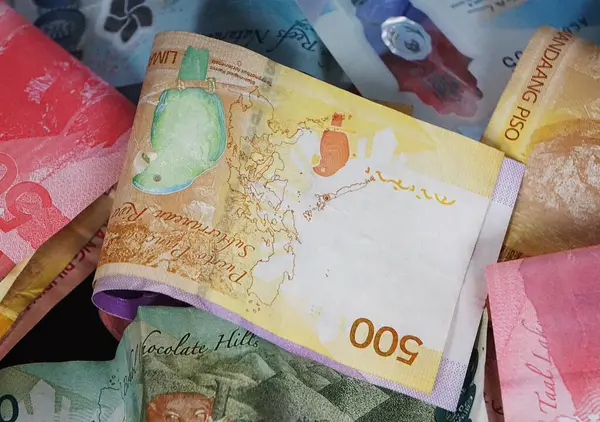 500 peso 'luk banknot, dağınık Filipin banknotlarının arka planında belirgin bir şekilde görünür, dinamik ve renkli bir para düzenlemesi yaratır..