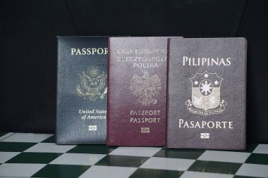 Yeşil bir satranç tahtasına koyu arkaplanı olan üç pasaport. Amerikan, Filipinli ve Polonya pasaportları birden fazla vatandaşlık ve küresel seyahat seçenekleri gösteriyor.