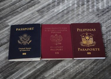 Üç pasaport, Amerikan Filipinlisi ve Polonyalı arka planı bulanık bir şekilde yan yana dizilmiş. Çoklu vatandaşlık ve uluslararası seyahat seçeneklerine örnek.