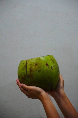 Açık, boş hindistan cevizi bir kadının ellerinde parlak bir arkaplan karşısında duruyor. Tropiklerle, sağlıklı yaşam tarzıyla ve doğal beslenmeyle bağlantılı egzotik meyveler..