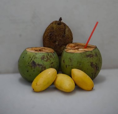 Marang, hindistan cevizi ve ön planda birkaç mango, bir pipetli hindistan cevizi. Bulanık arka plan, tropikal ve egzotik bir hava yaratıyor..