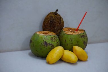 Ön planda, marang meyvesi, iki hindistan cevizi ve bulanık arka planı olan bir mango. Doğal, tropikal bir ortamda egzotik ve taze meyvelerin bileşimi..