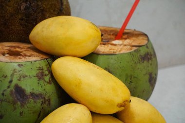 Mango ön planda, iki kesik hindistan cevizi ve bir marang meyvesi ile, bulanık bir arka plan üzerine kurulmuş. Doğal ve tropik bir atmosferde egzotik meyveler..