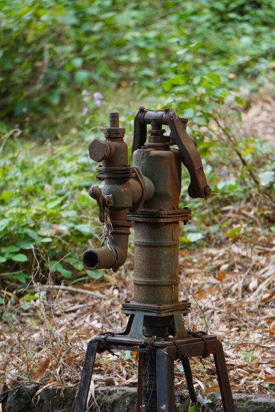 An old rural water hydrant with water gushing out, used for manual water pumping in the countryside. A rustic scene showing traditional village access to water.