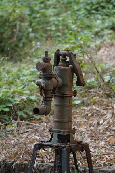 An old rural water hydrant with water gushing out, used for manual water pumping in the countryside. A rustic scene showing traditional village access to water.