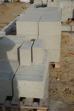 Cement blocks on pallets at a construction site, ready for building a house, organized materials, foundations and walls, realistic construction site view, construction work, construction crew.