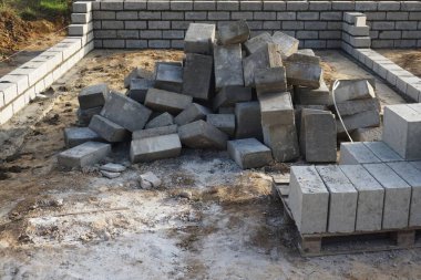 Cement blocks on pallets at a construction site, ready for building a house, organized materials, foundations and walls, realistic construction site view, construction work, construction crew.