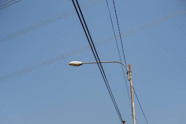 Üzerlerinde kablolar olan sokak lambaları. Sokak lambası fotoğrafı. Mavi gökyüzünün altında sokak ışıkları.