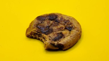 Isırılmış çikolatalı kurabiye. Sol tarafında ısırık izi olan kurabiyeler sarı arka planda izole edilmiş.