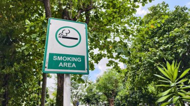 a green sign indicating a designated smoking area. tree and sky background