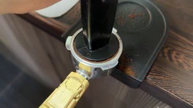Özel bir paspasın üzerinde bir kurcalayıcı kullanarak taze öğütülmüş kahveyi iskele filtresine sıkıştıran kadın ellerinin yakın çekimi. Espresso için hazırlık aşaması bir ev kahvecisi ayarında.