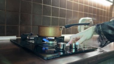 Bir tencere gaz sobasının üzerinde düz olmayan bir alevle duruyor. Metal bir alet, ocağı sabit bir aleve ayarlamak için kullanılır. Mutfak ortamında çekilmiş..