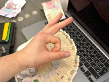 Bir el, dizüstü bilgisayarı ve 500 tane UAH banknotuyla masanın önünde iyi bir jest yapıyor. Başarı kavramı, mali istikrar veya çevrimiçi kazanç.