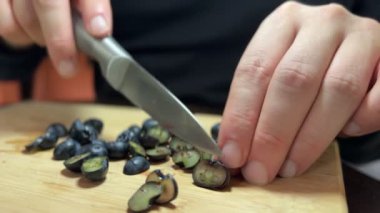 Bir insan ahşap kesme tahtasıyla farklı boyutlarda taze yaban mersini keser. Böğürtlenli bir konteynır yakınlarda duruyor. Yaz meyvesi, sağlıklı ve mevsimlik atıştırmalıklar.